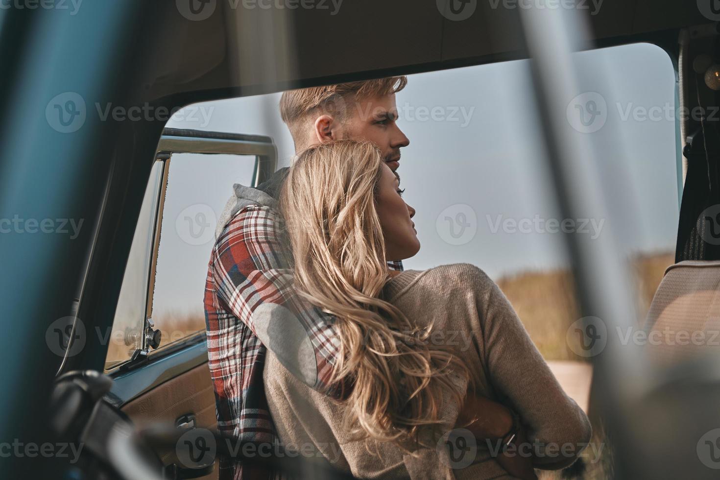 Always protecting her... Beautiful young couple embracing while standing outdoors near the retro style mini van photo