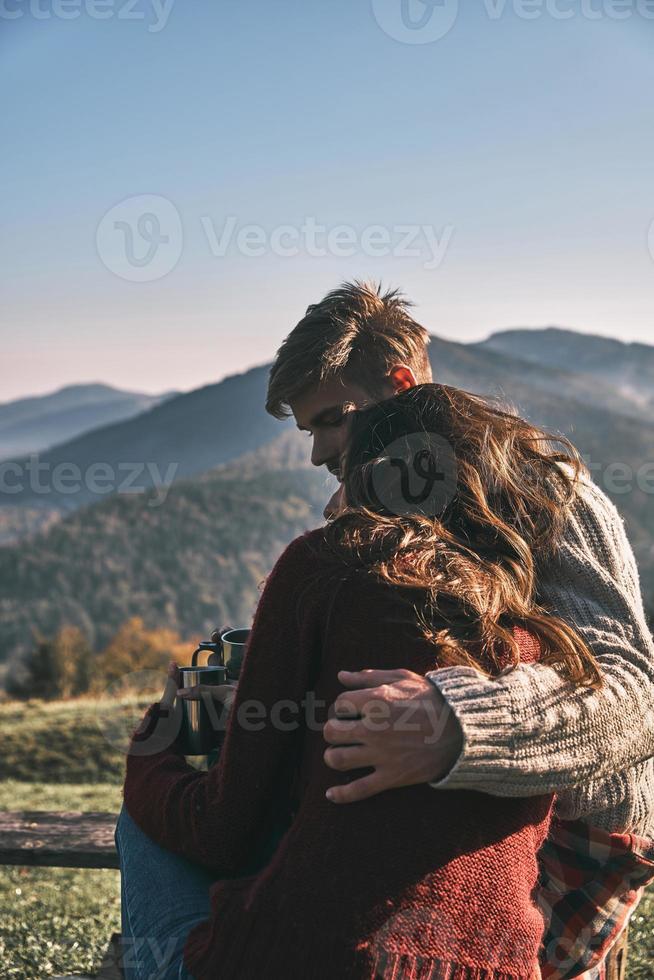 Close relationships. Beautiful young couple having morning coffee while spending carefree time in mountains photo