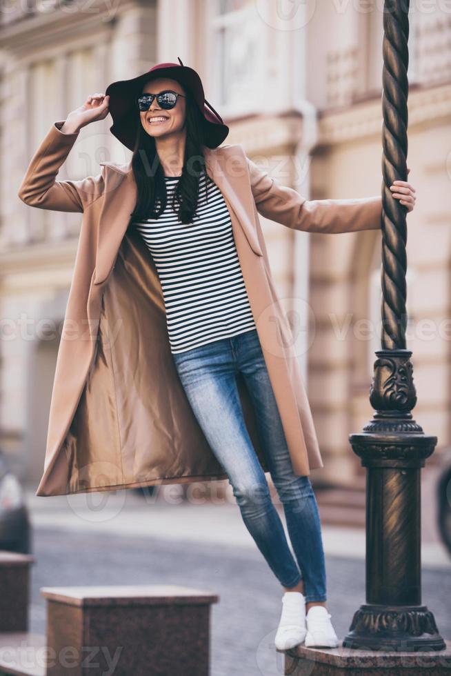 amando esta ciudad. bella joven con gafas de sol ajustando su sombrero mientras se apoya en la farola al aire libre foto