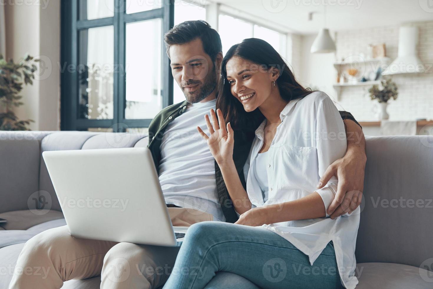 Beautiful young couple drinking coffee and looking on the laptop while sitting on the sofa at home photo