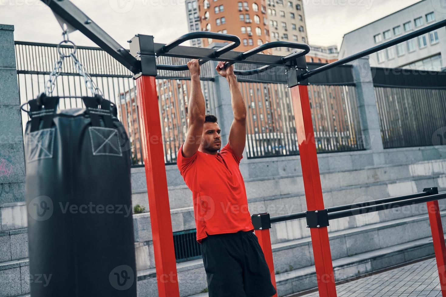 Handsome young man in sports clothing doing pull ups while exercising outdoors on the city street photo
