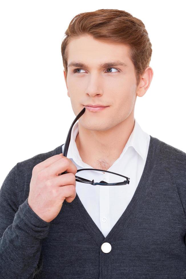 Full of creative ideas. Thoughtful young man holding glasses near mouth