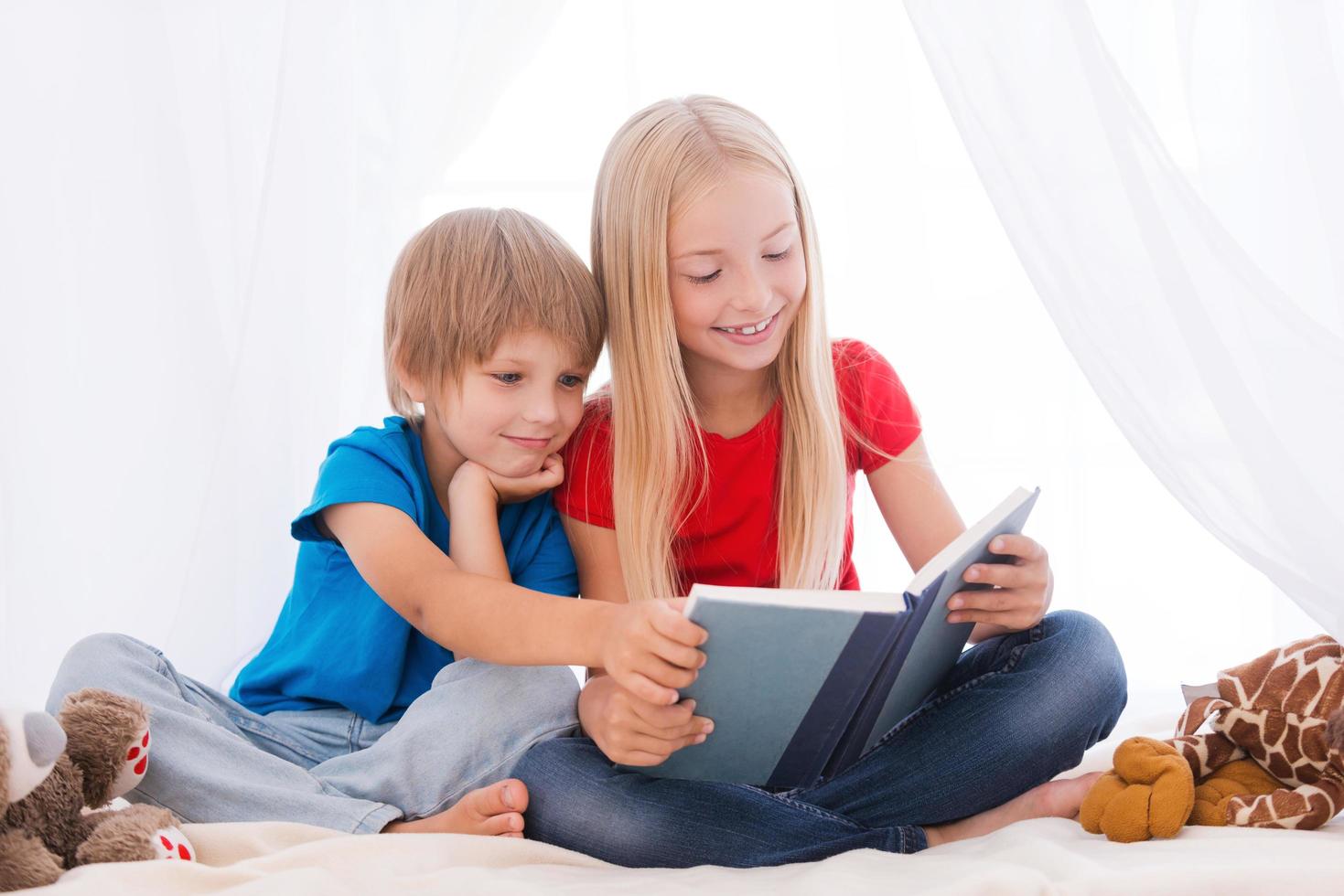 leyendo un libro emocionante. dos lindos niños leyendo un libro juntos mientras se sientan juntos en la cama foto