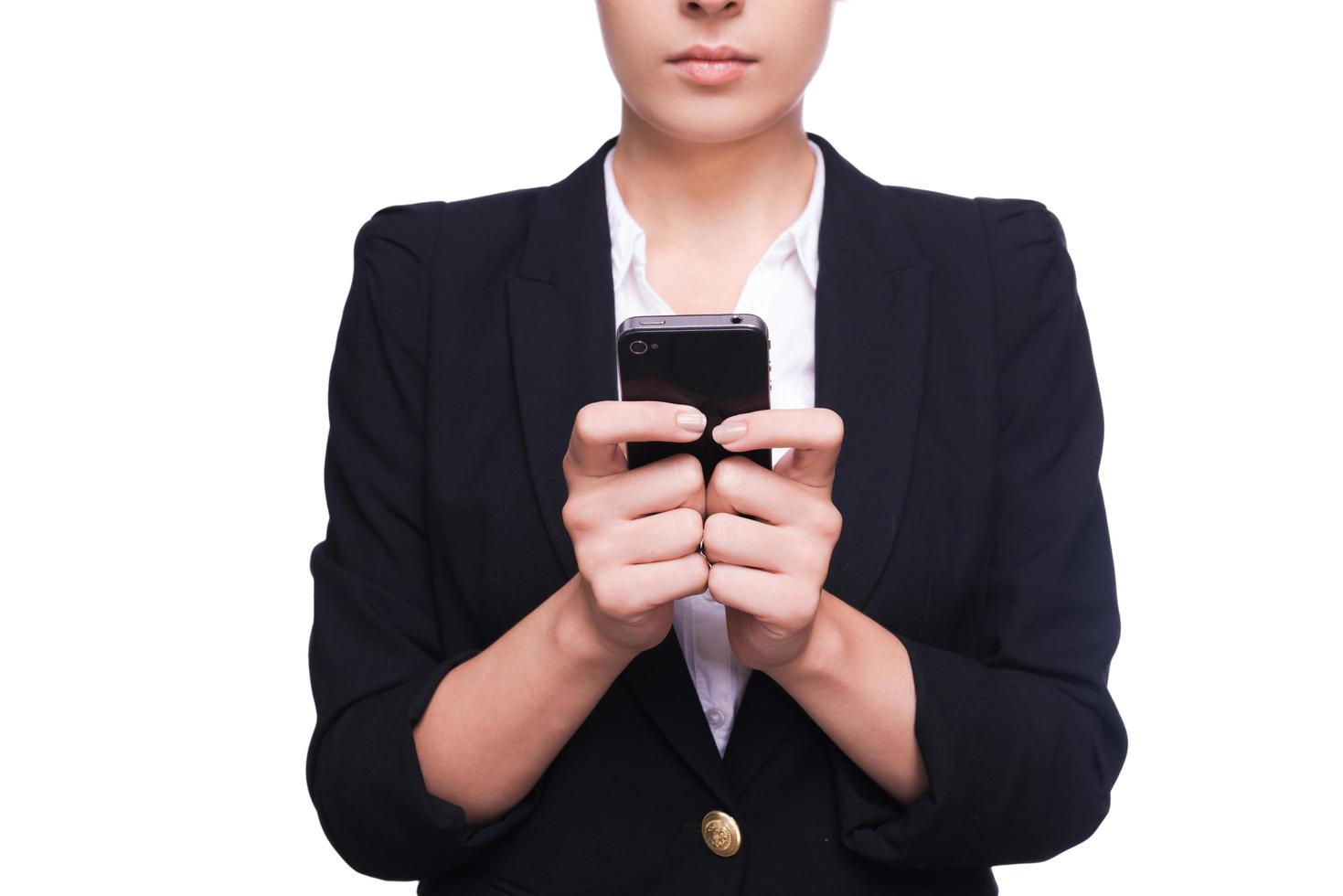 Typing business message. Close-up of young woman in formalwear holding mobile phone while standing isolated on white photo