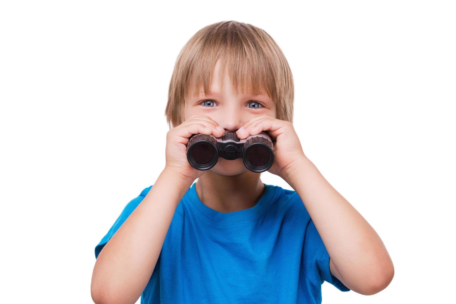 Little boy with binoculars. Cheerful little boy looking at camera and smiling while holding binoculars near face standing isolated on white photo