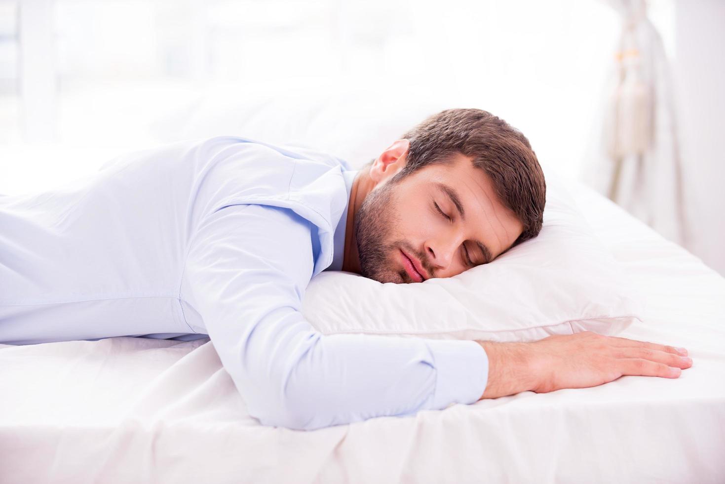 Tired and overworked. Handsome young man in shirt sleeping in bed photo