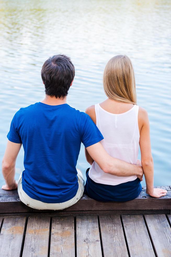 Romantic date. Rear view of young loving couple sitting at the quayside together photo