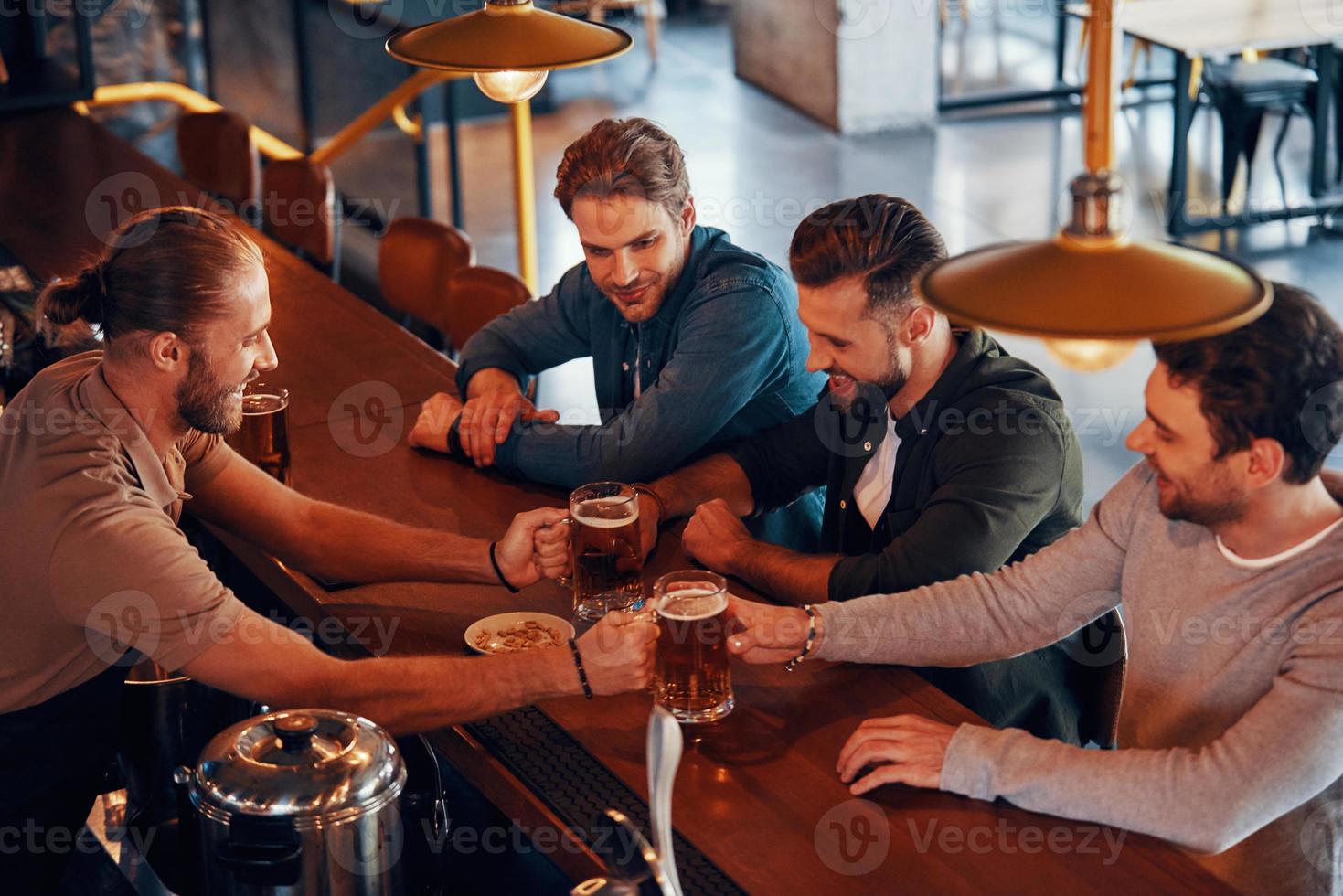 Top view of bartender serving beer to young men while standing at the bar counter in pub photo