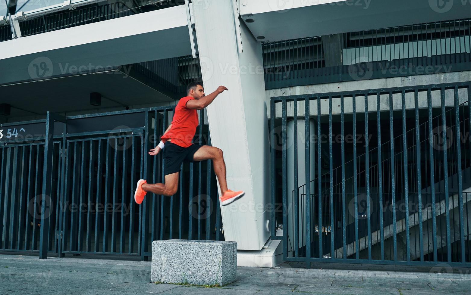 Full length of confident young woman in sports clothing hovering in a long jump while exercising outdoors photo