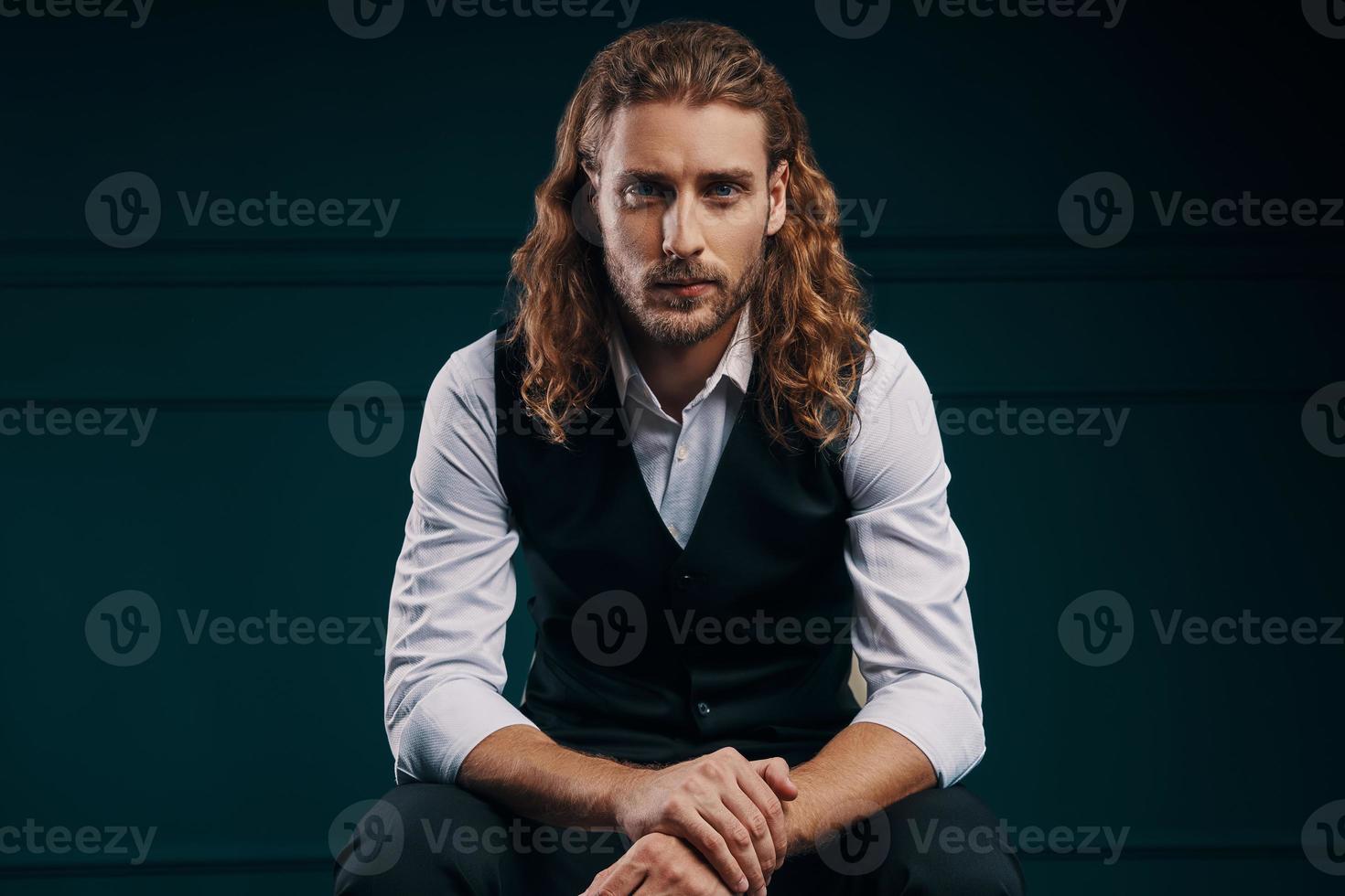 Stylish young man in elegant shirt looking at camera while sitting against green background photo