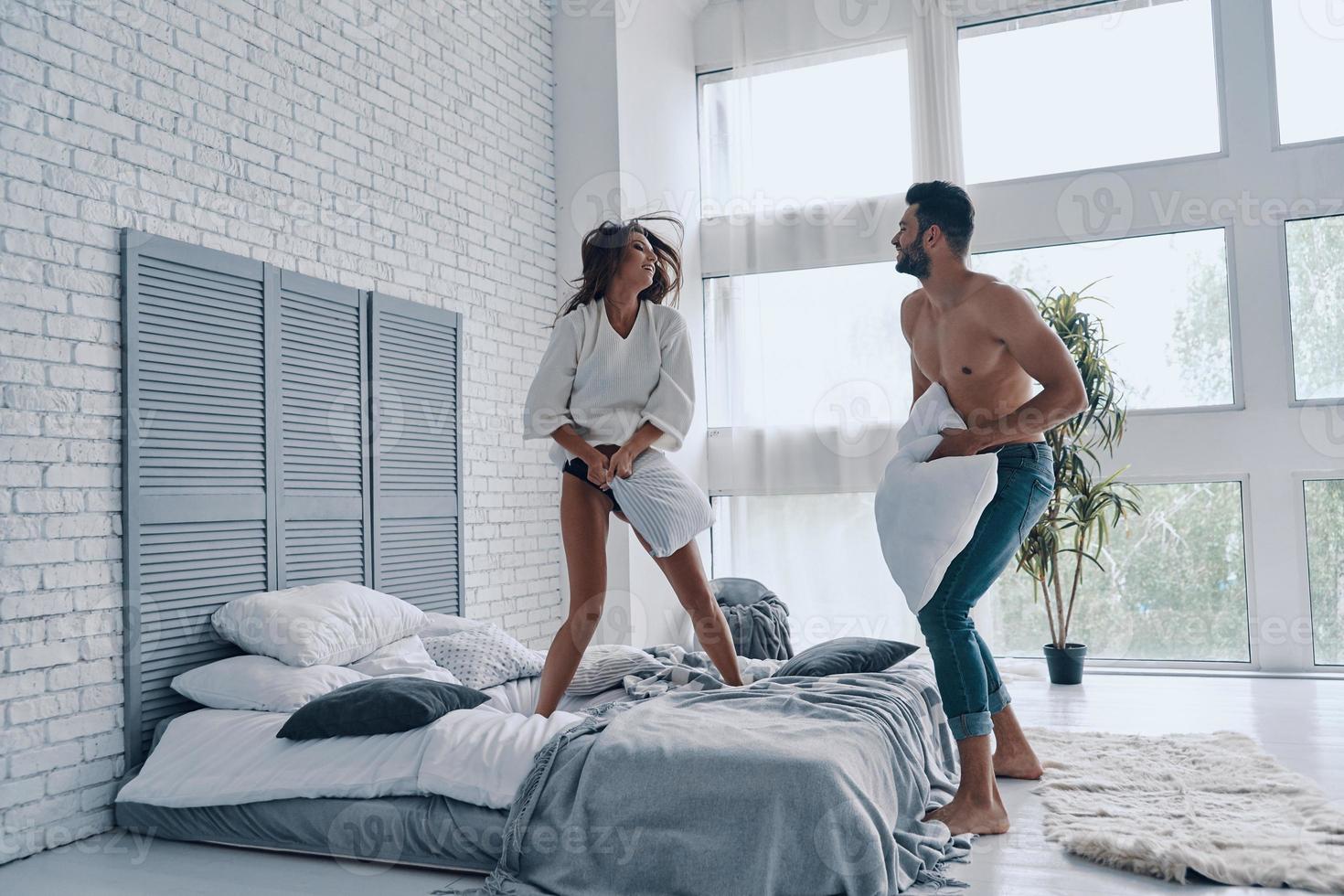 Crazy in love. Full length of happy young couple having a fun pillow fight while spending carefree time in the bedroom photo