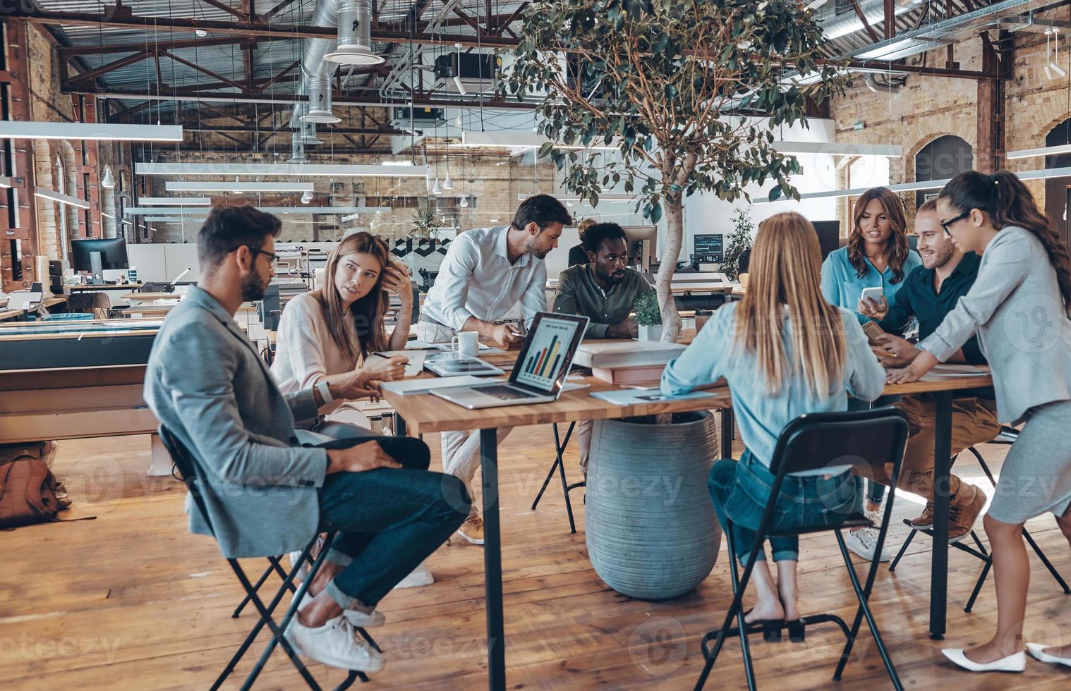Group of young modern people in smart casual wear communicating and using modern technologies while working in the office photo