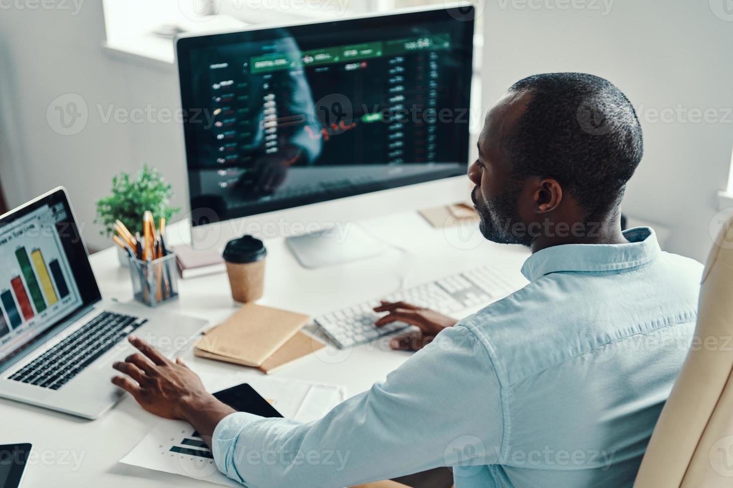 Rear top view of young African man in shirt using computer while working in the office photo