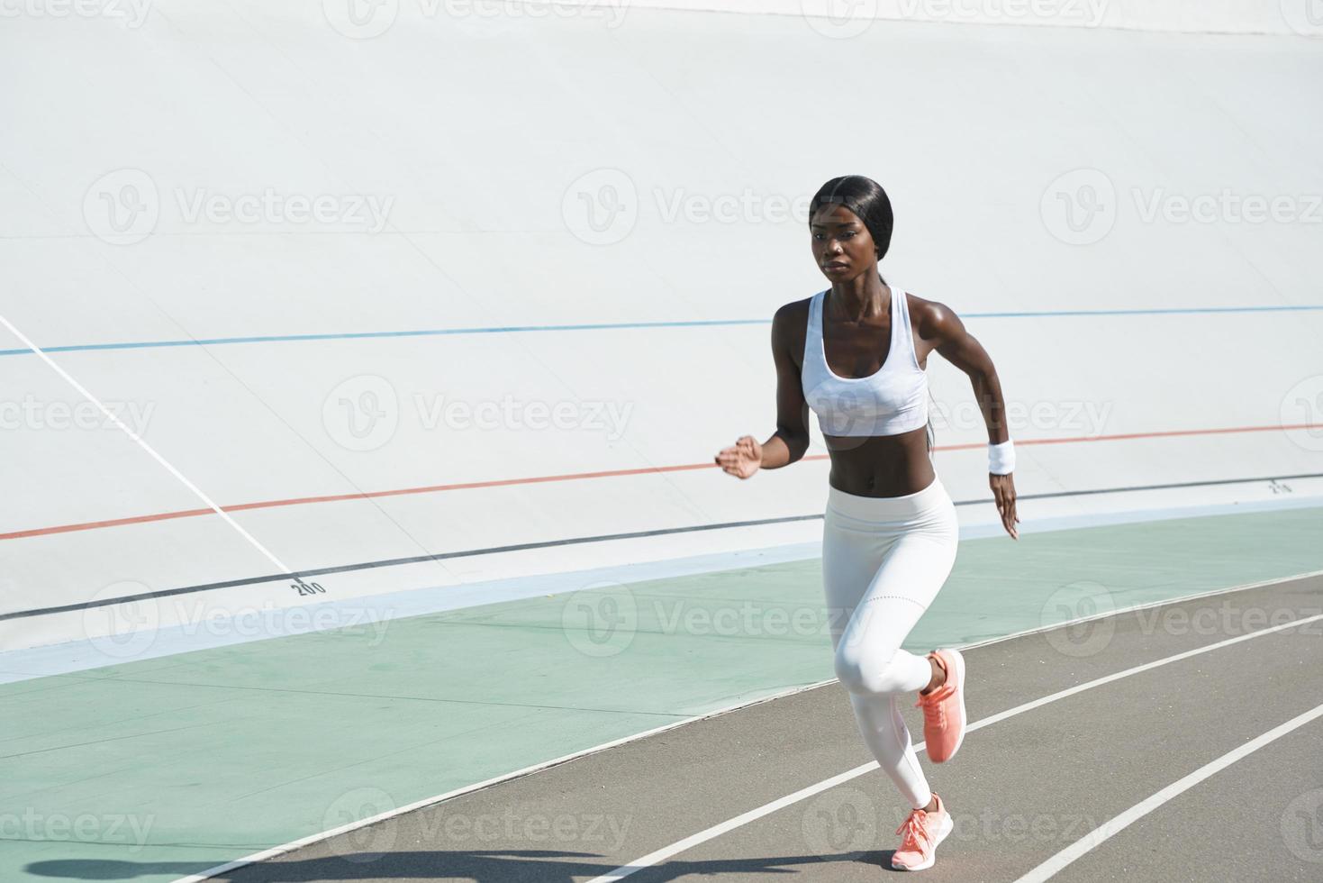 confiada joven africana en ropa deportiva corriendo en la pista al aire libre foto