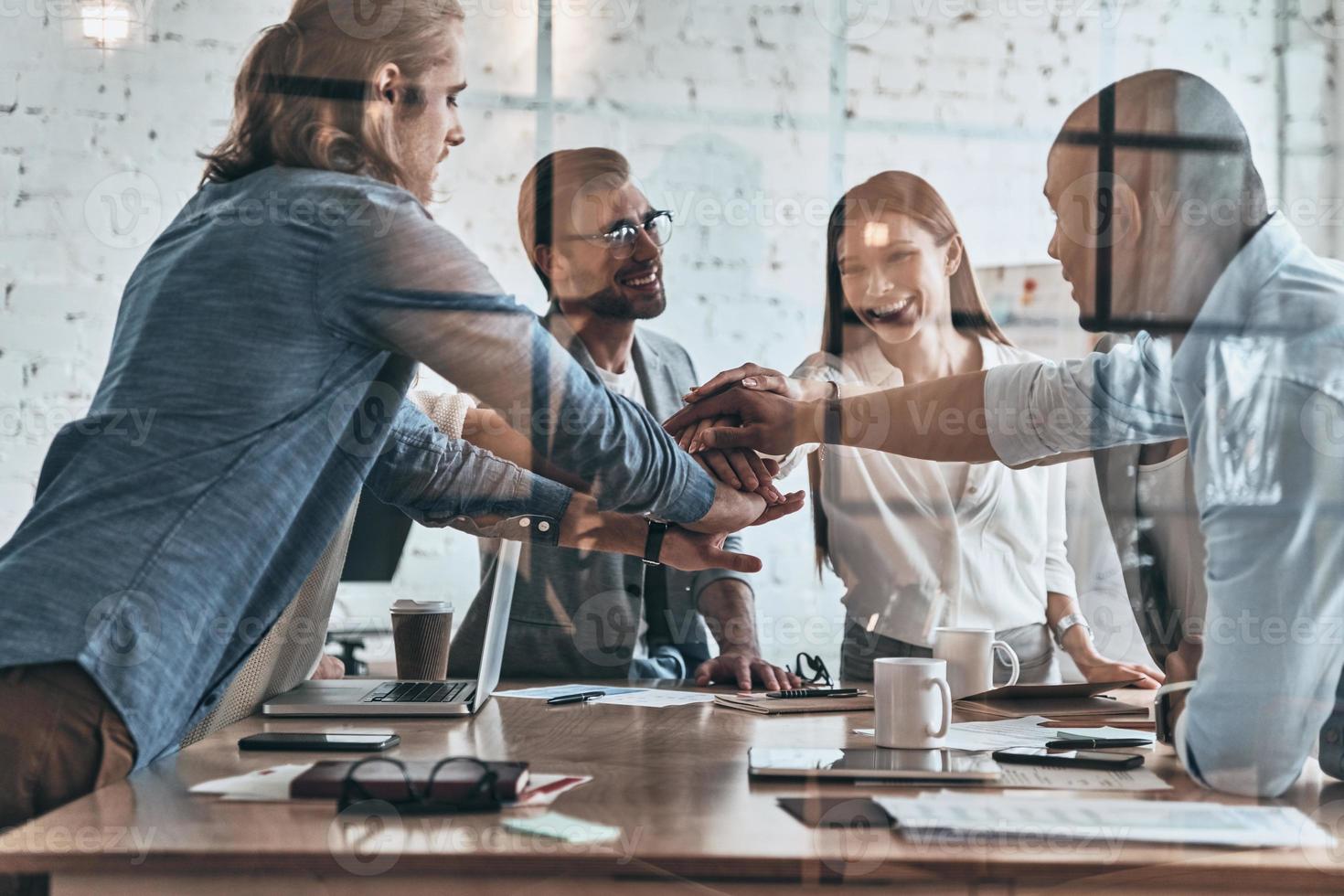 Successful team. Diverse group of business colleagues holding hands on top of one another in a symbol of unity while working behind the glass wall in the board room photo