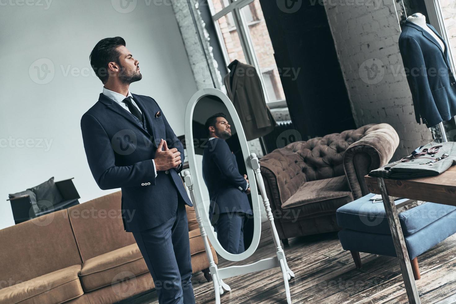 Looking just perfect. Handsome young man in full suit looking away while standing indoors photo