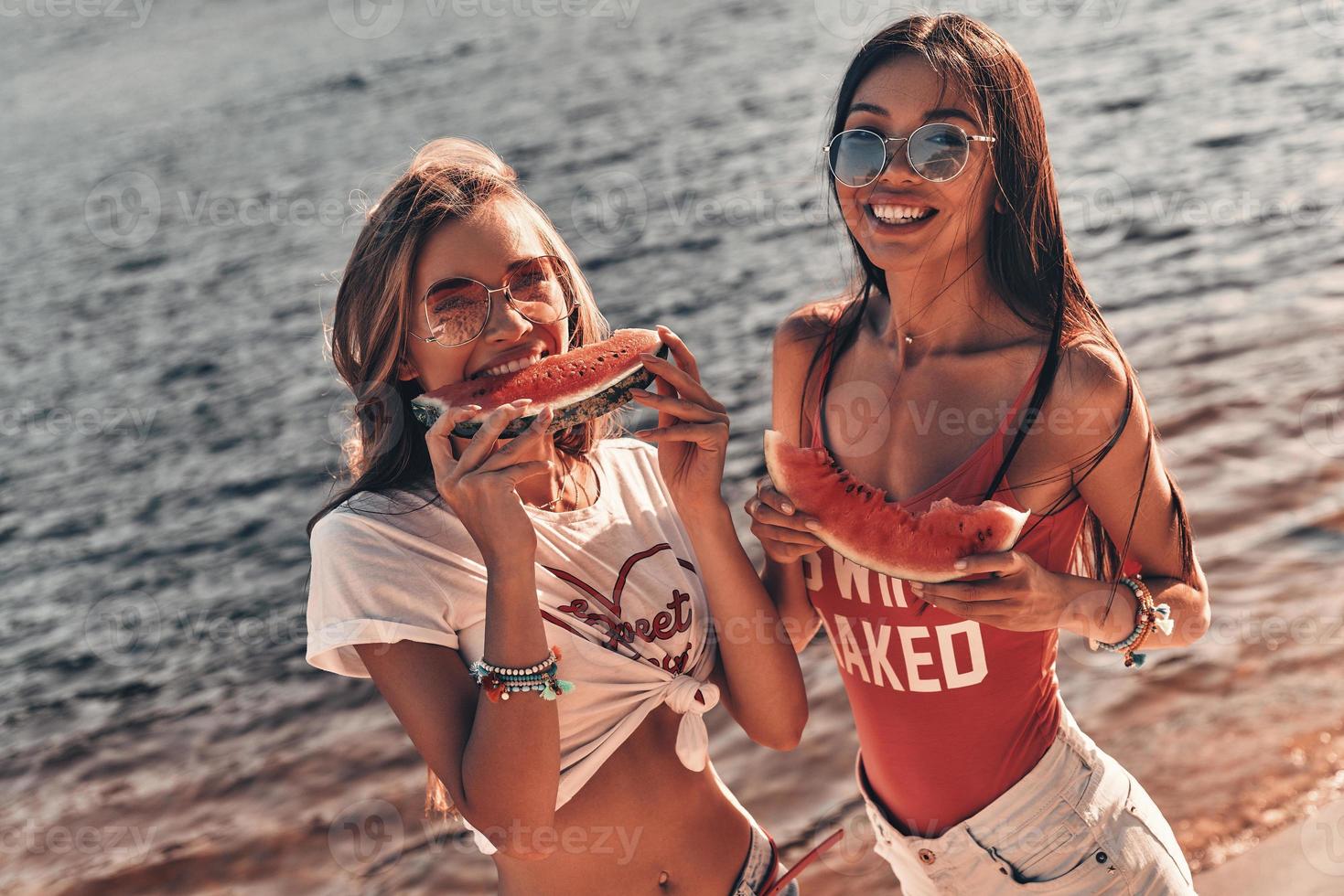 Summer relaxation. Top view of attractive young women smiling and eating watermelon while standing near the river photo