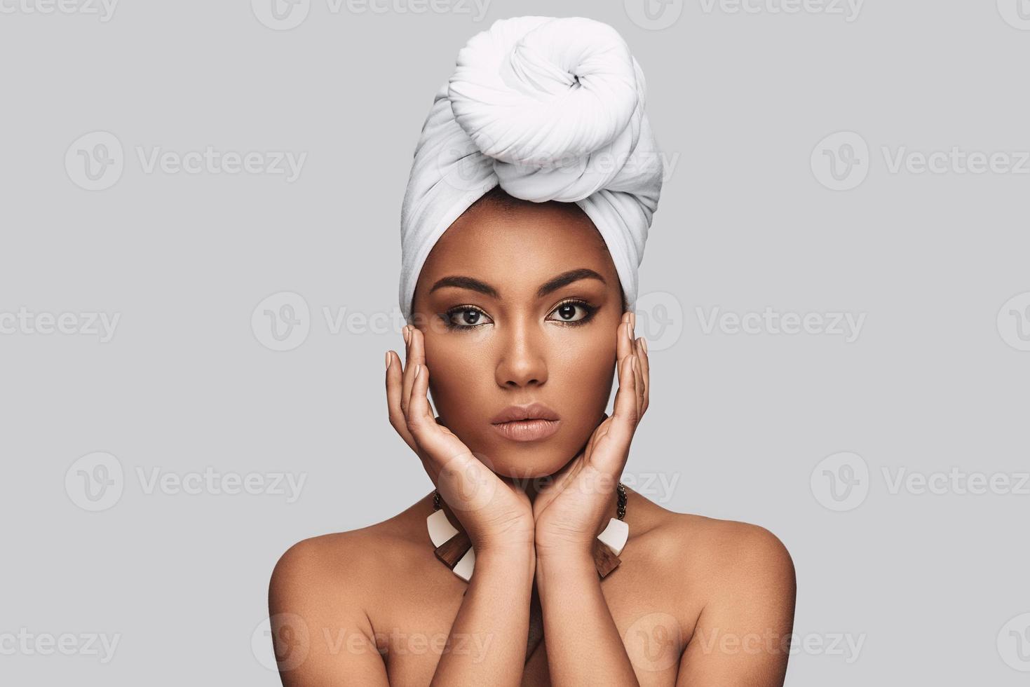 African tradition. Attractive young African woman in turban looking at camera while standing against grey background photo