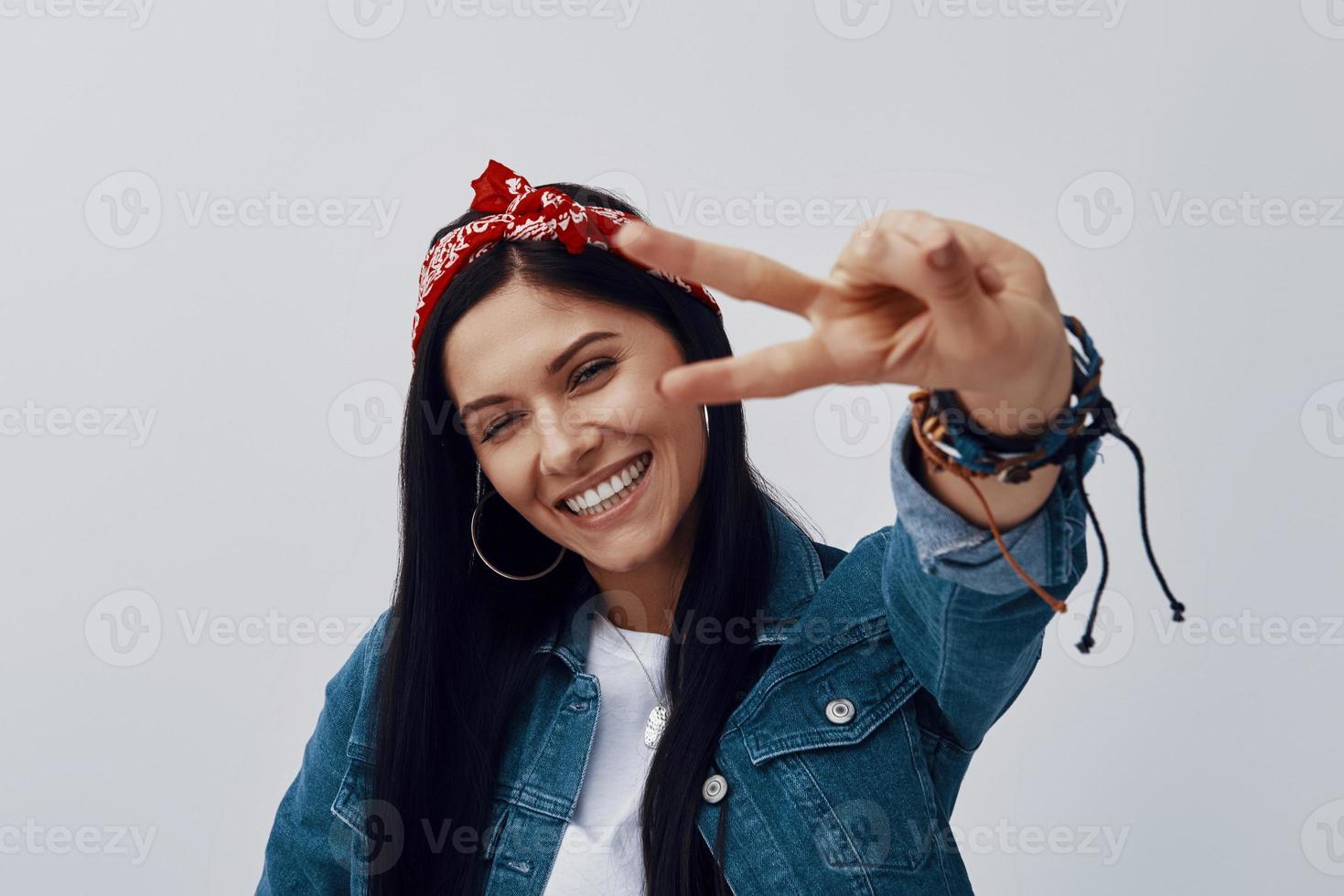 Funky young woman in bandana looking at camera and gesturing while standing against grey background photo