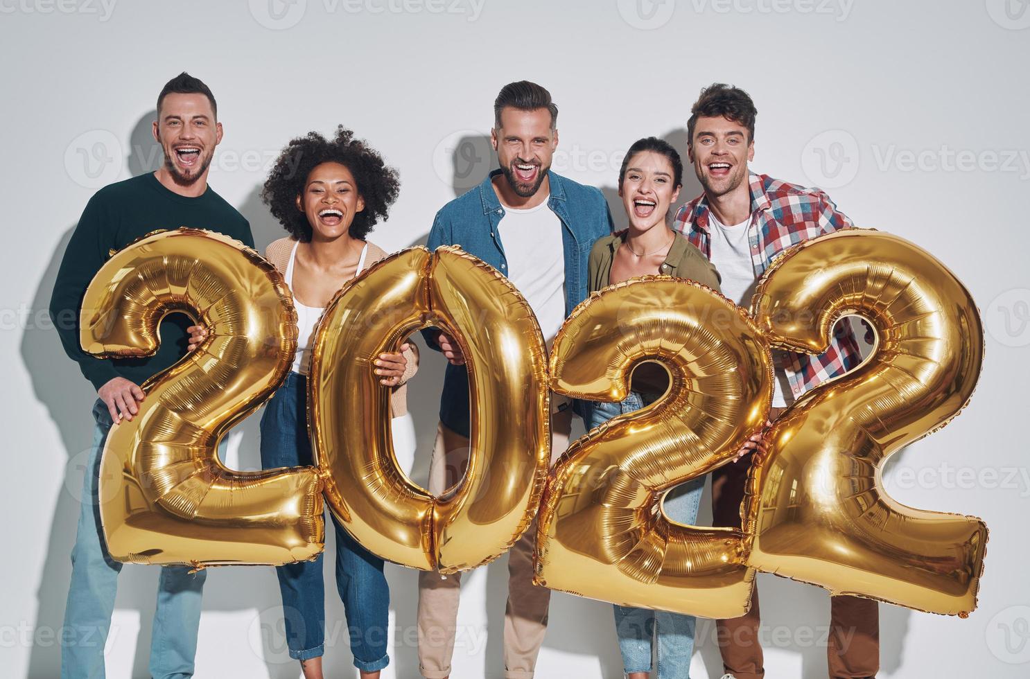 Group of young beautiful people in casual clothing carrying gold colored numbers  and smiling photo