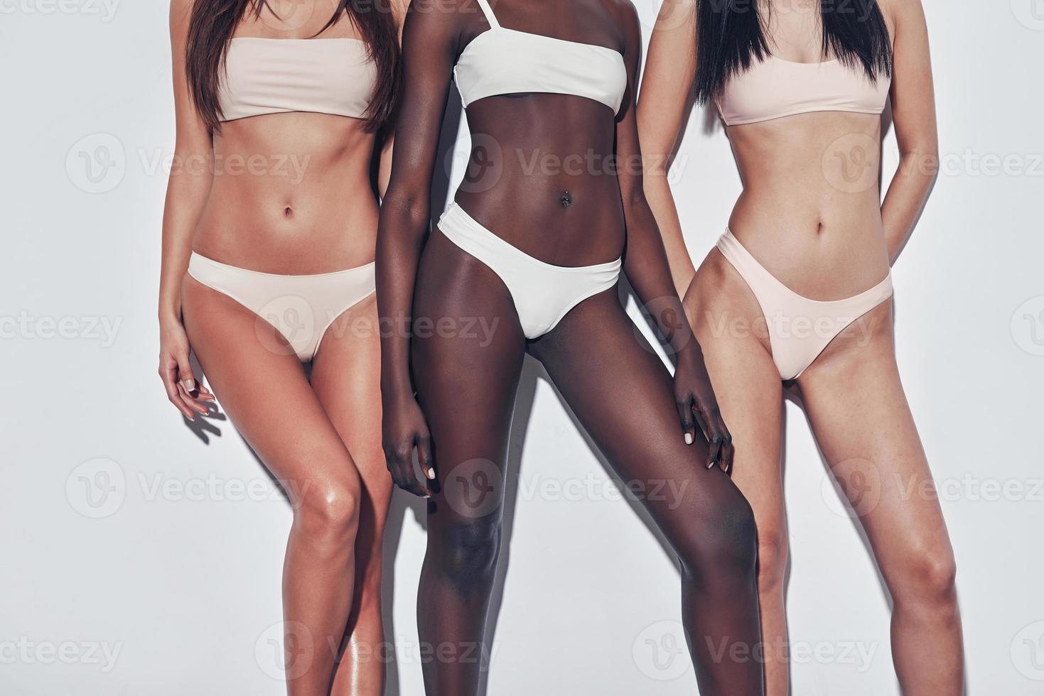 Naturally fit and beautiful. Close up of three attractive mixed race women in lingerie standing against grey background photo