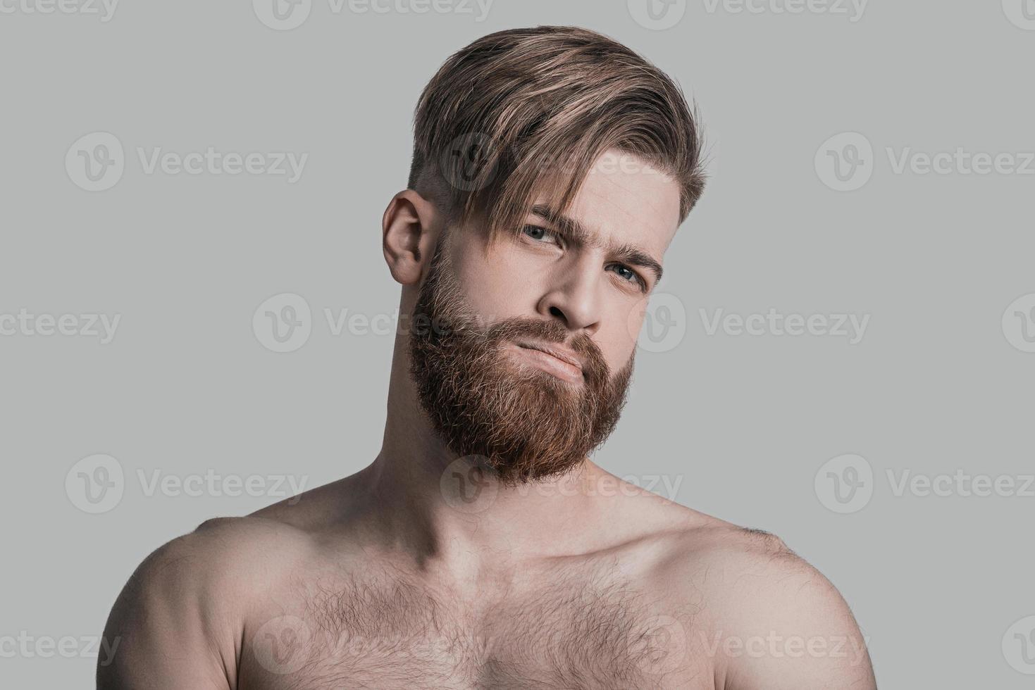 Feeling suspicious. Portrait of young attractive man looking at camera while being in front of grey background photo
