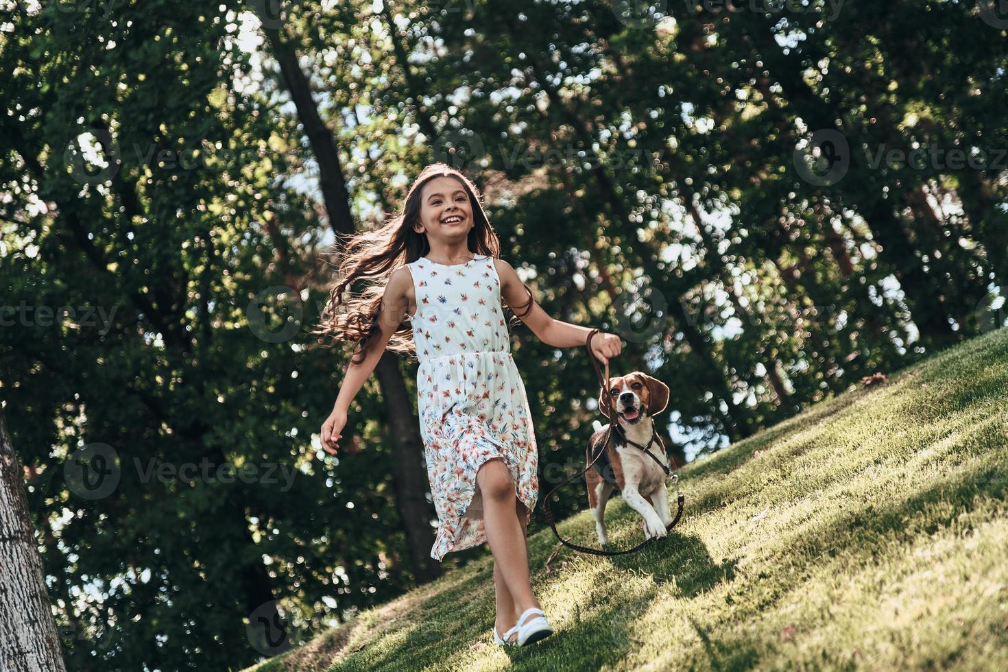 Full length of cute little girl playing with her dog and smiling while running outdoors photo