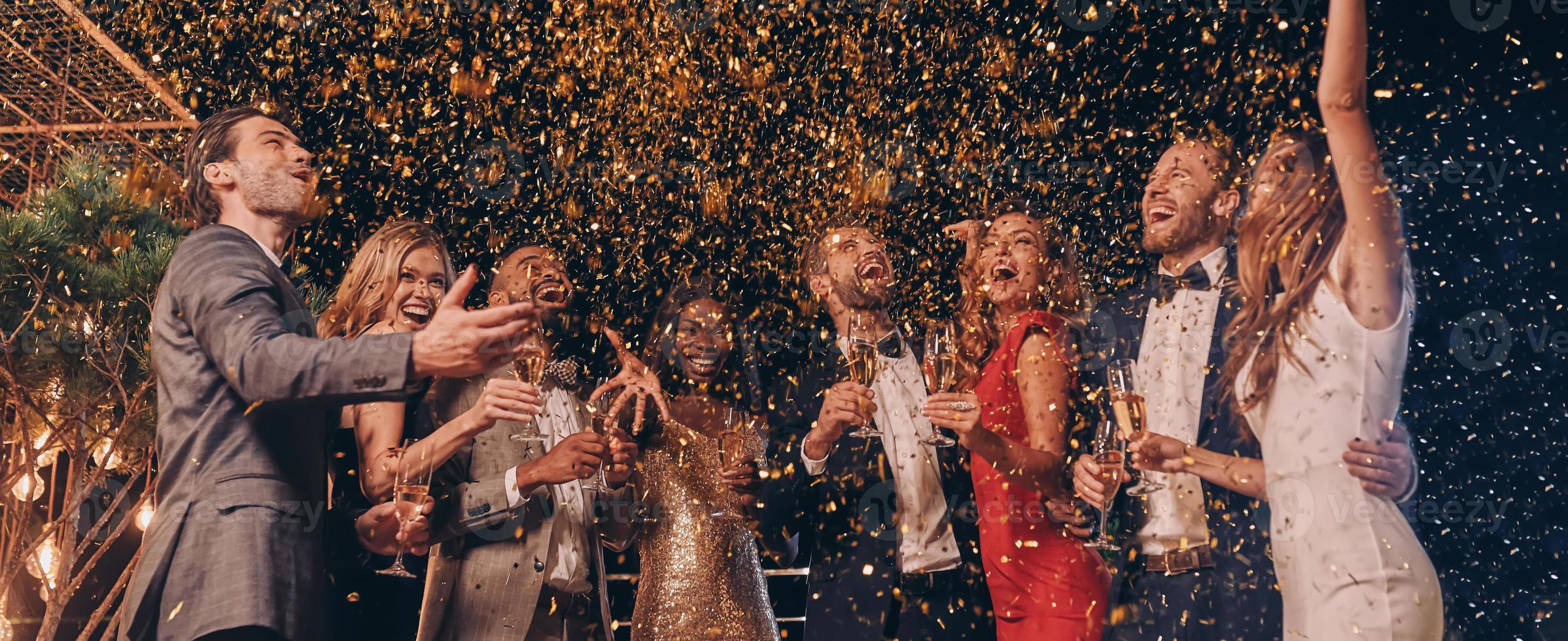 Group of happy people in formalwear having fun together with confetti flying all around photo