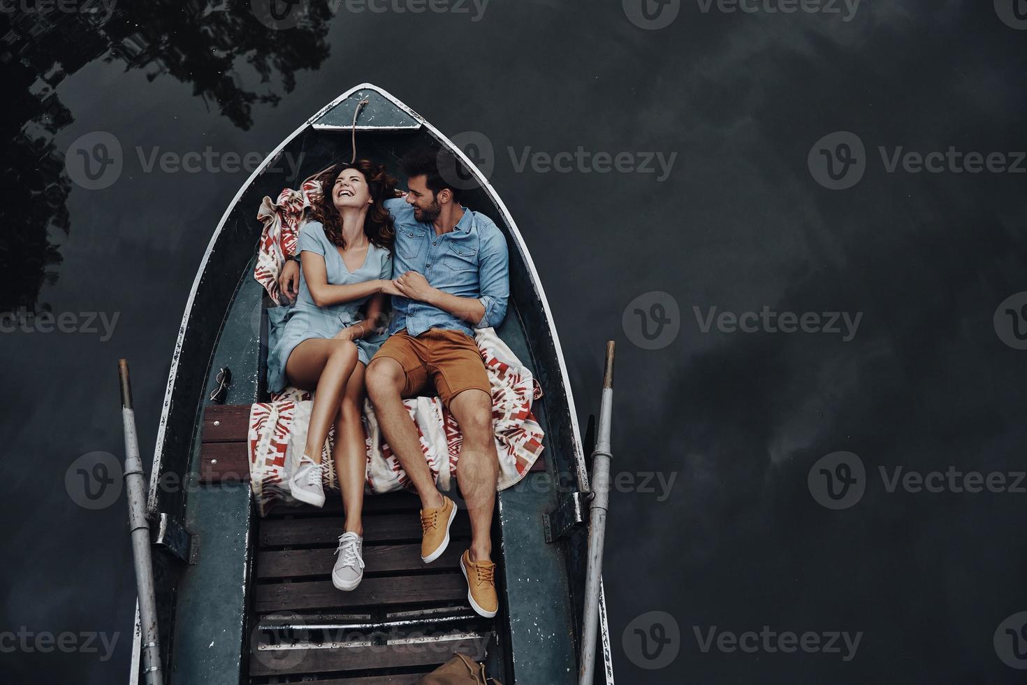 Feeling just happy. Top view of beautiful young couple embracing and smiling while lying in the boat photo