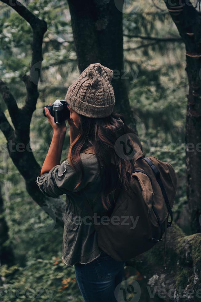 Nice shot. Young modern woman with backpack photographing nature while hiking in the woods photo