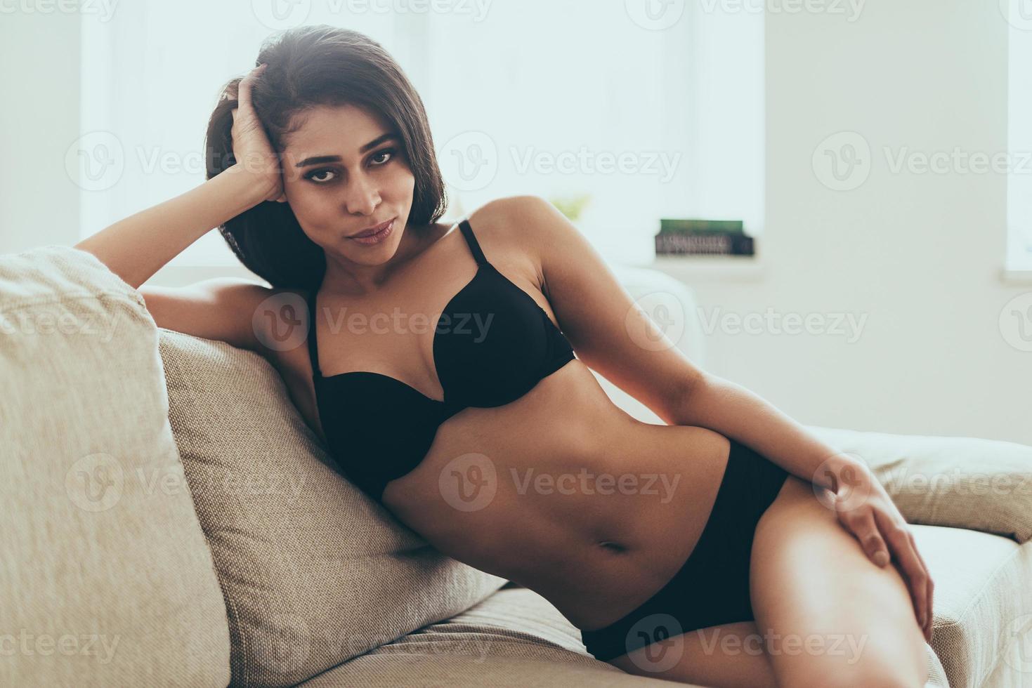 Sweet seductress. Beautiful young mixed race woman in black lingerie  looking at camera while sitting on couch at home 13500964 Stock Photo at  Vecteezy