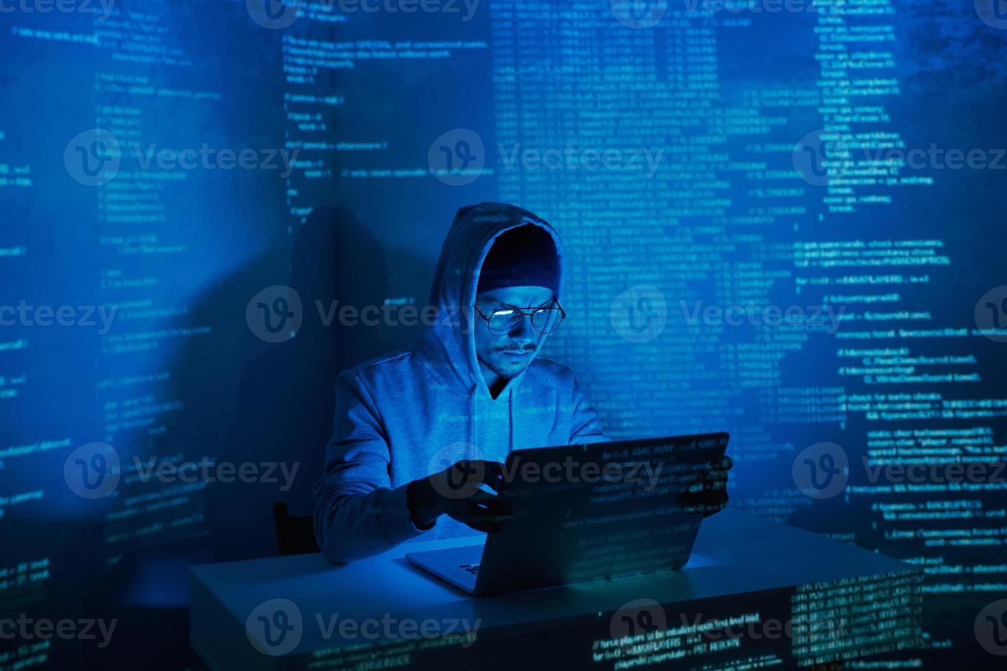 Young man in hooded shirt using computer against dark background photo