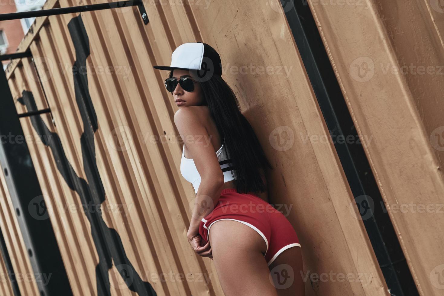 confiada en su cuerpo perfecto. bella joven con uniforme deportivo mirando por encima del hombro mientras está de pie al aire libre foto