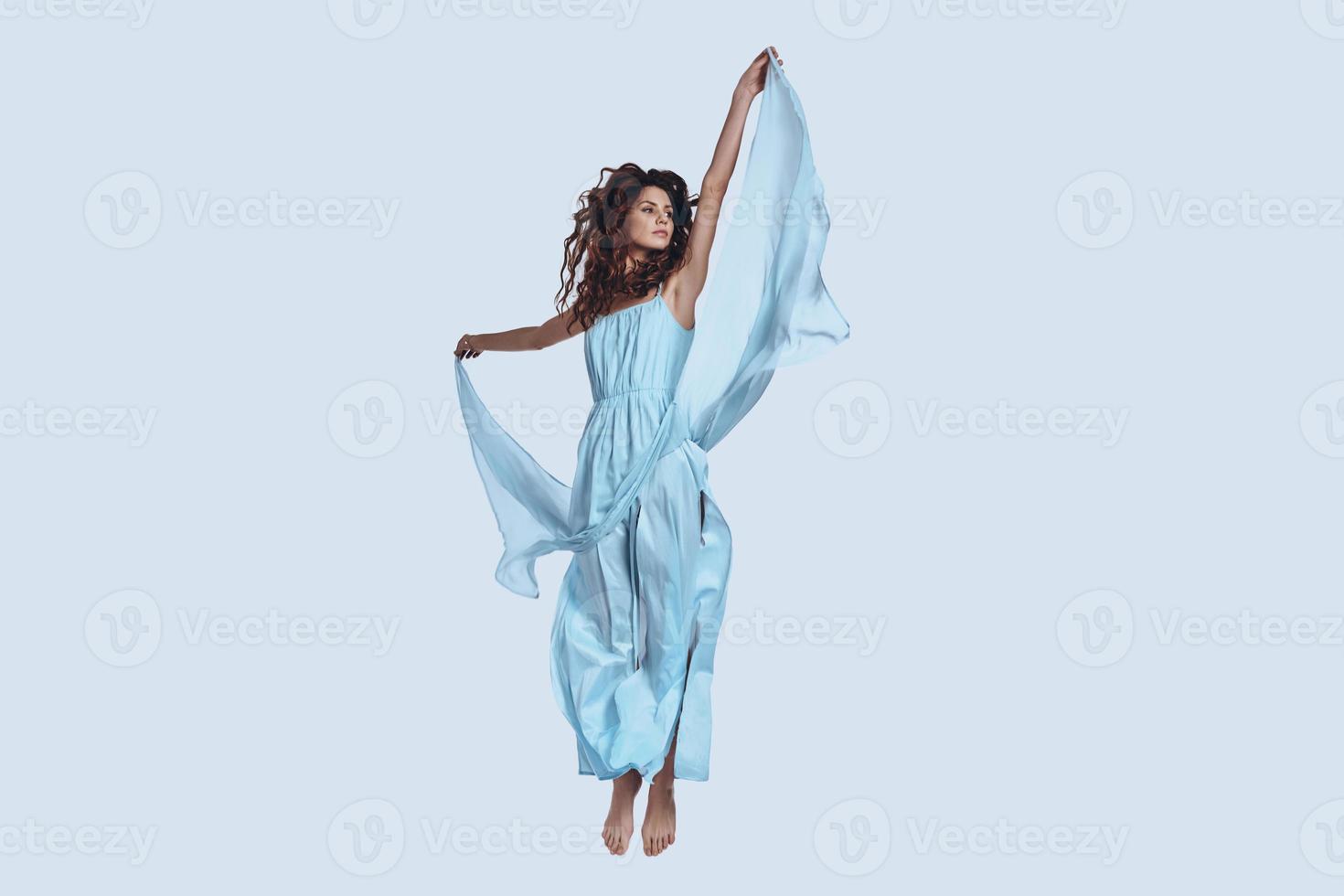 Pure perfection. Full length studio shot of attractive young woman in elegant dress looking away while hovering against grey background photo