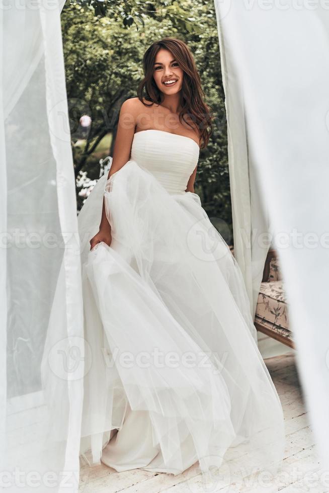 Best day ever. Full length of attractive young woman in wedding dress looking at camera and smiling while standing outdoors photo