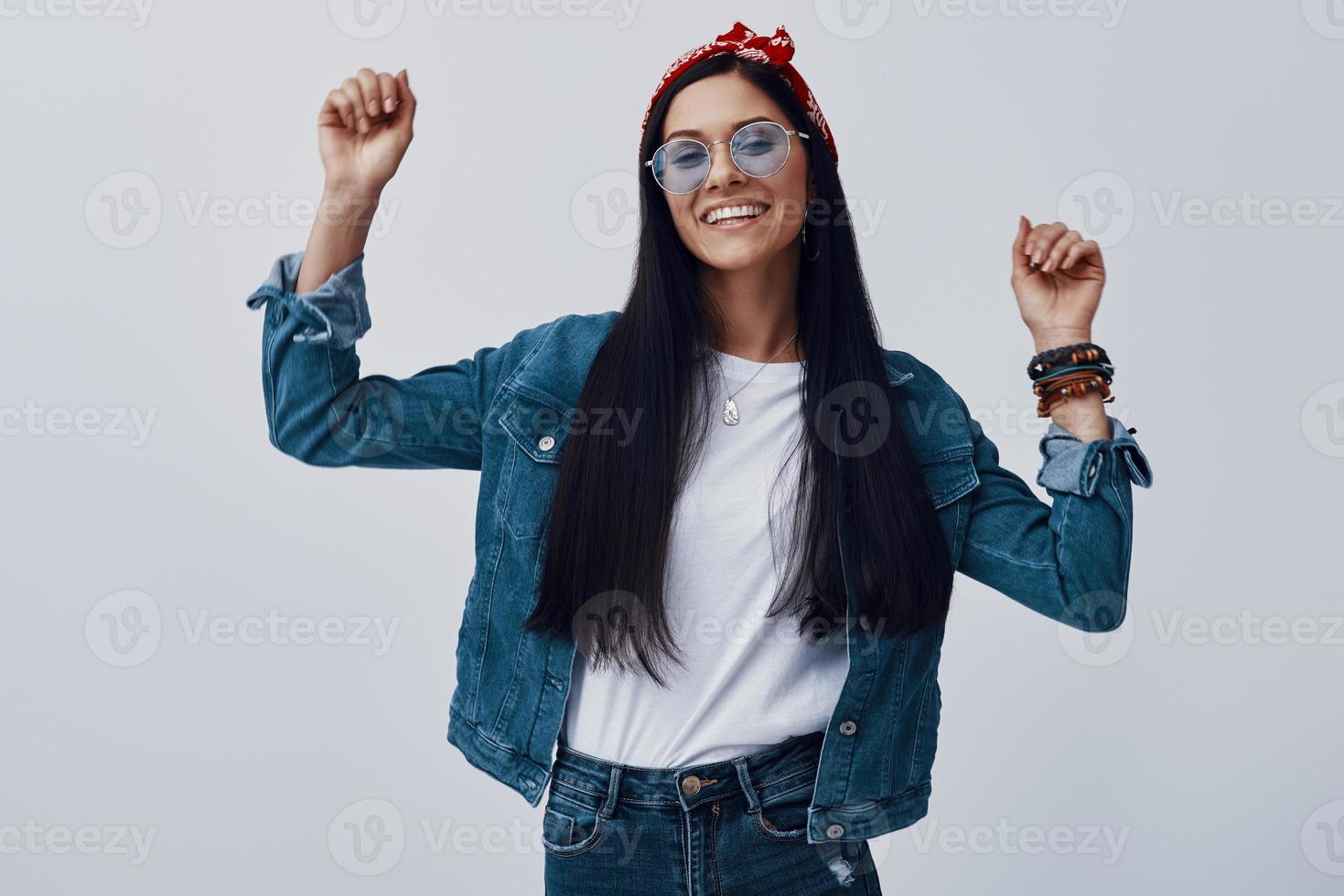 Attractive young woman in eyewear and bandana smiling while standing against grey background photo