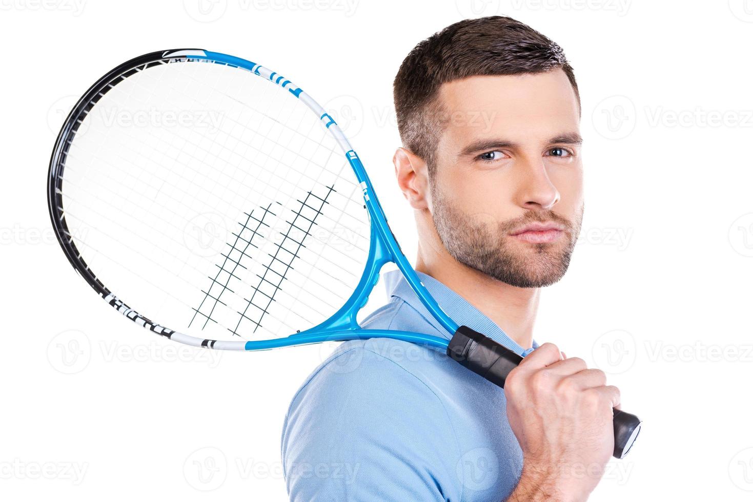Ready to play. Confident young man holding tennis racket and looking at camera while standing against white background photo