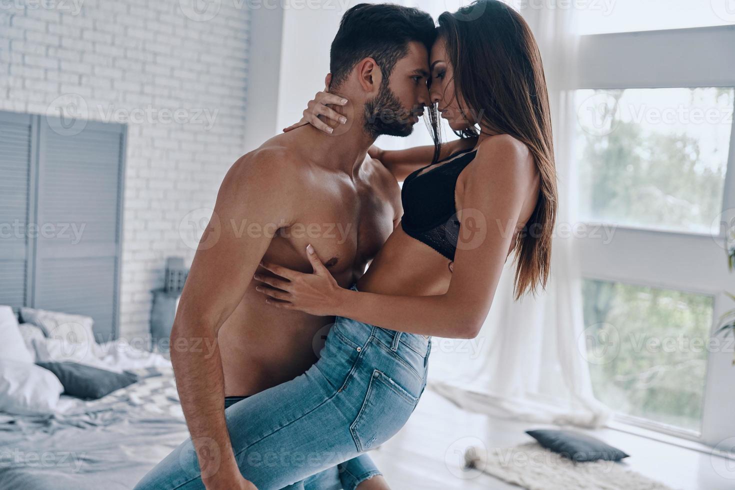 Passion. Handsome young shirtless man carrying semi-dressed attractive woman while standing in the bedroom photo