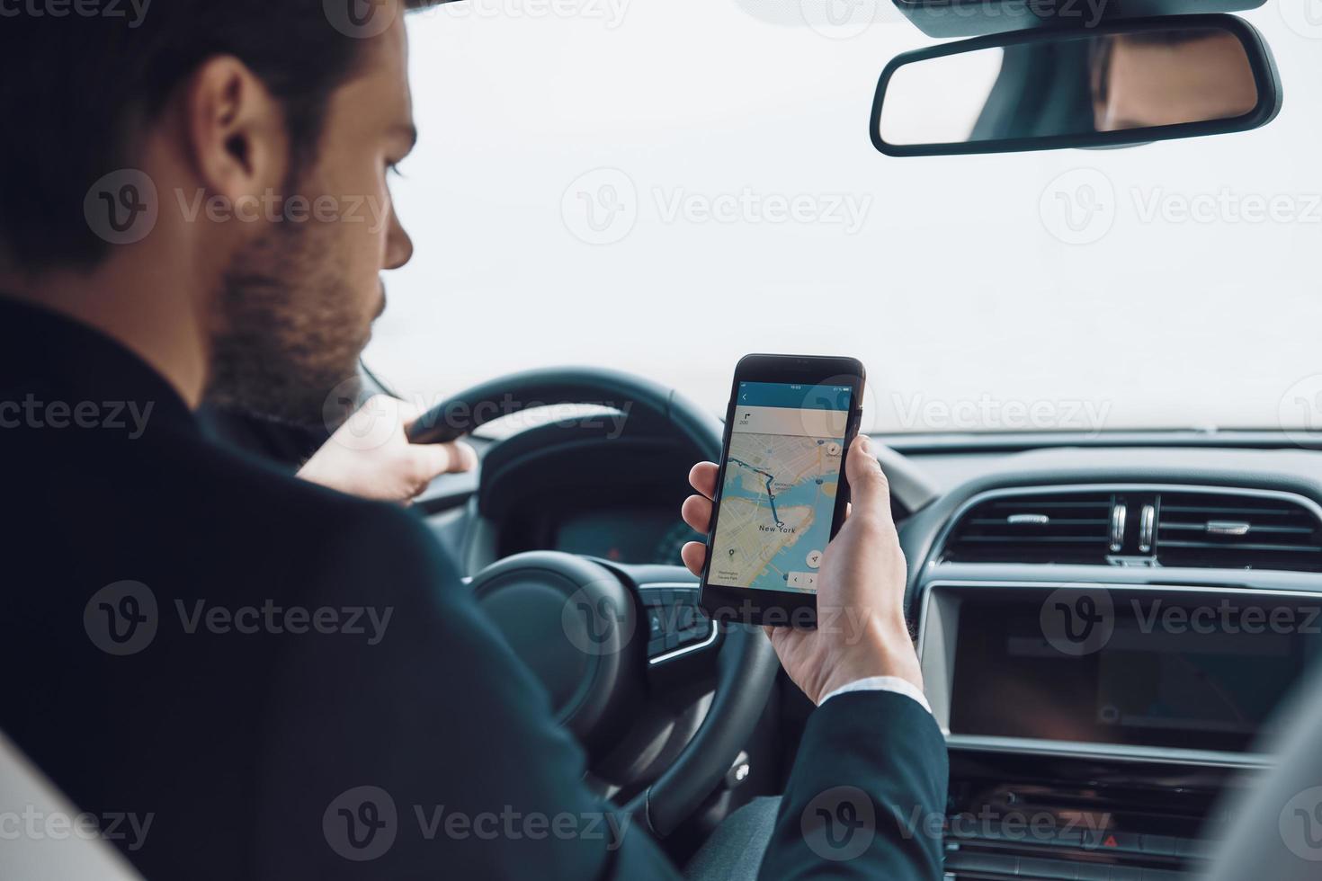 Checking the right way. Rear view of young man using smart phone to check the map while driving a car photo