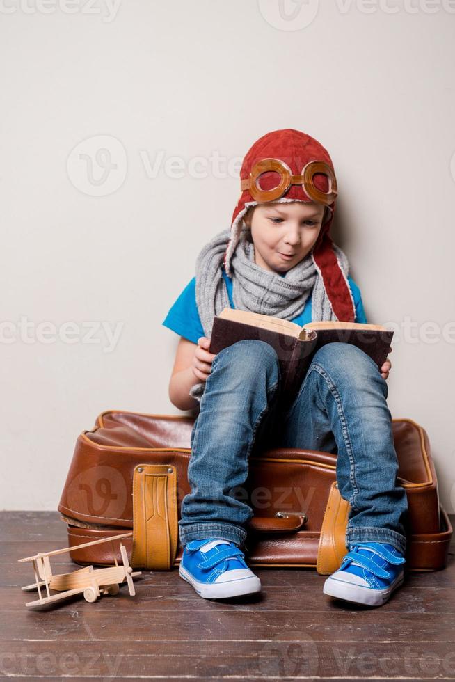 listo para grandes viajes. niño feliz con sombreros de piloto y anteojos que lleva un maletín grande y sonríe foto