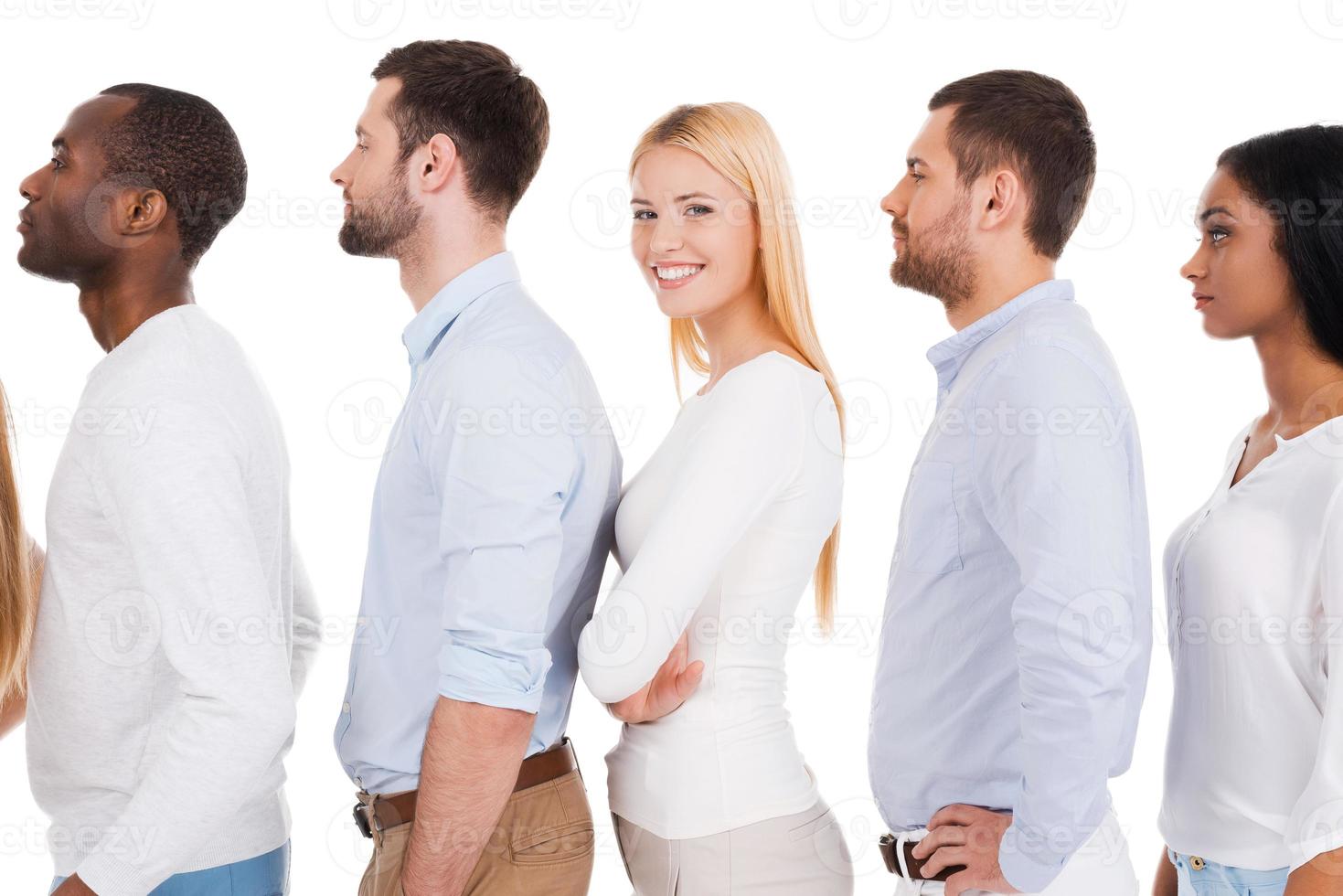 todos tendrán una oportunidad. vista lateral de una hermosa joven mirando la cámara y sonriendo mientras está de pie en una fila con otras personas y contra el fondo blanco foto