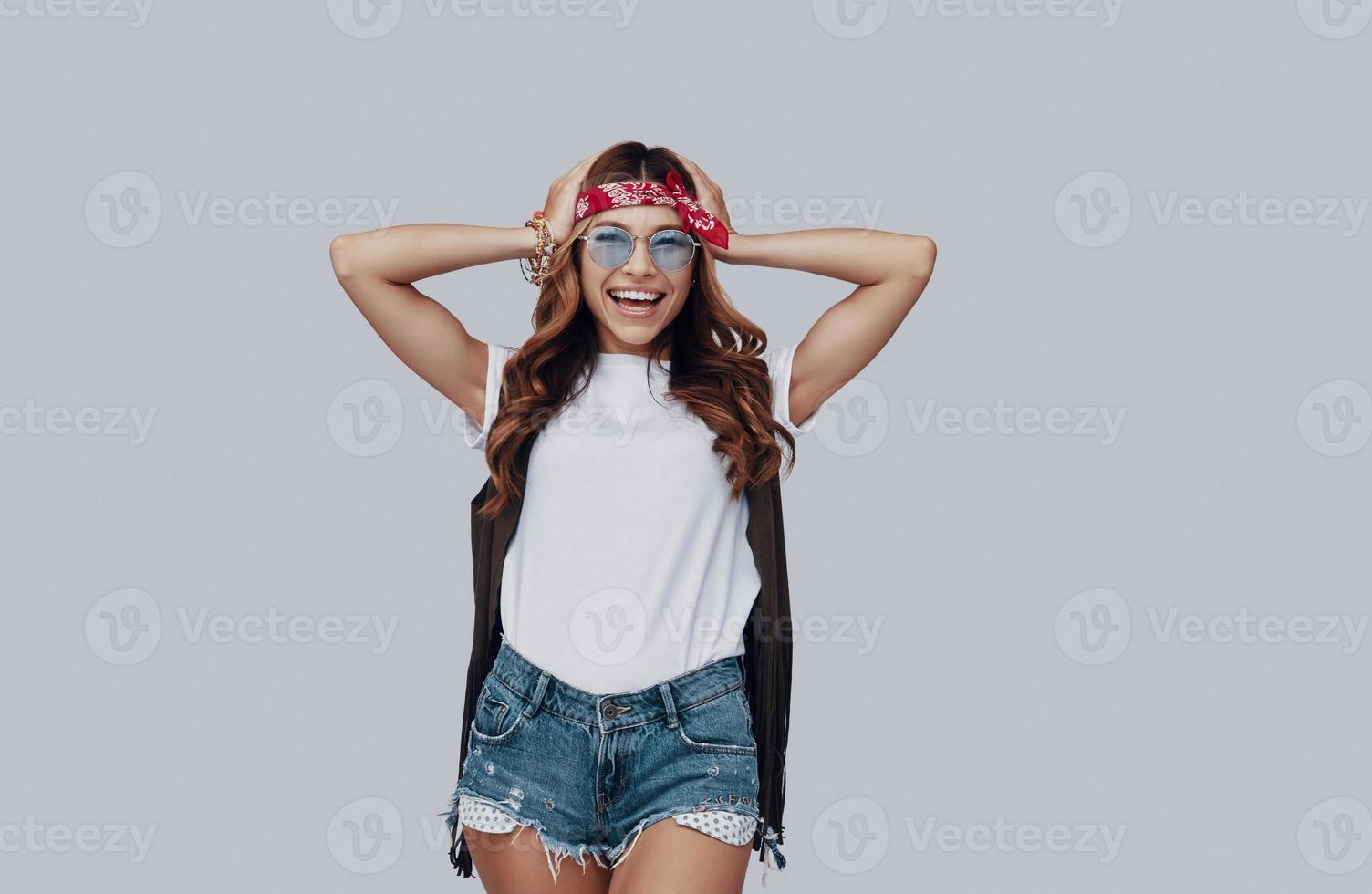 Attractive stylish young woman looking at camera and smiling while standing against grey background photo