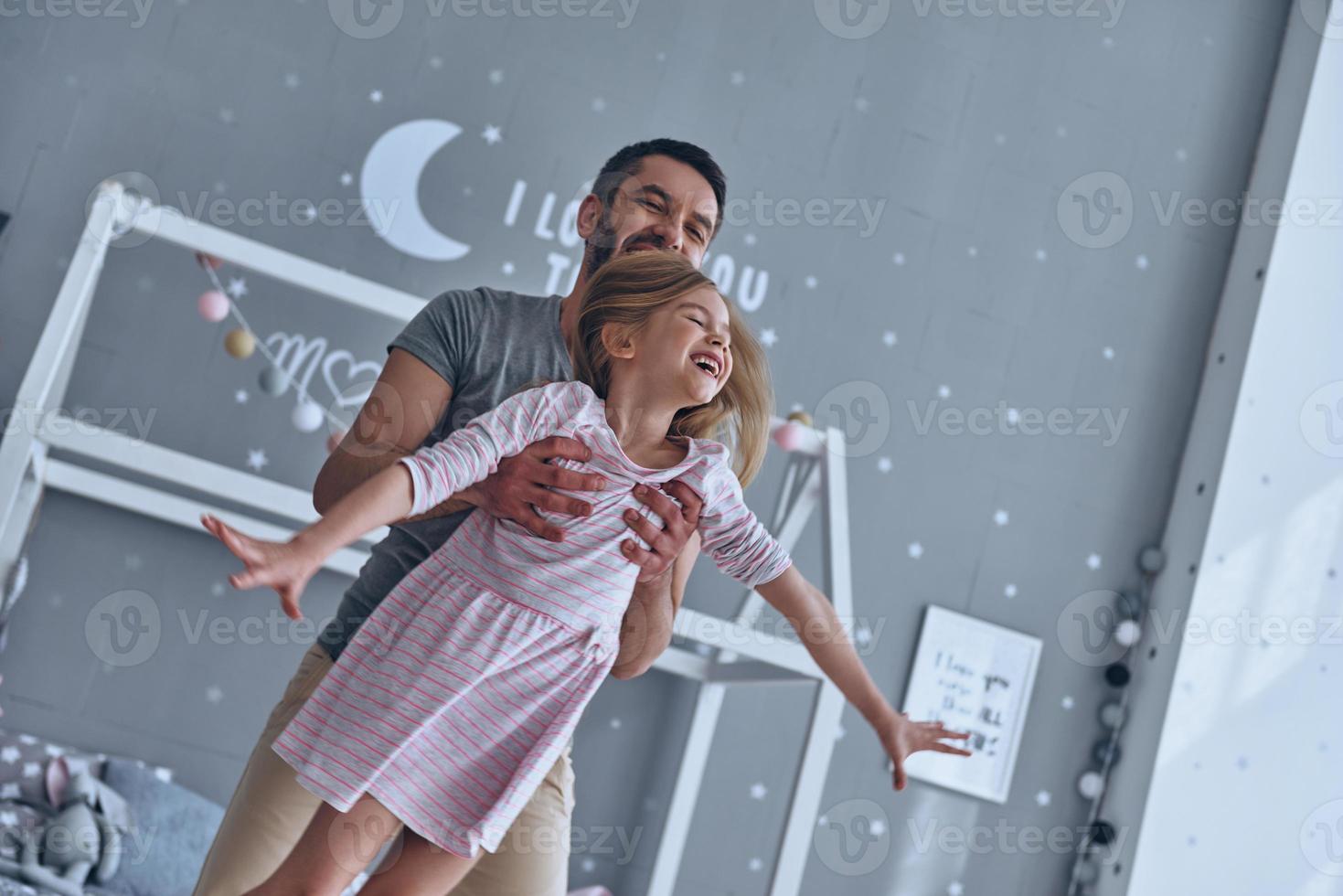 Sincere joy. Young loving father carrying his daughter and smiling while spending free time at home photo