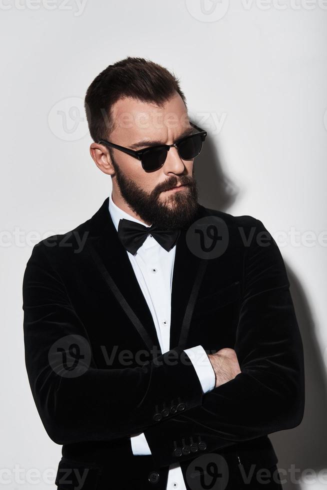 Feeling confident in his style. Handsome young man in full suit keeping arms crossed while standing against grey background photo