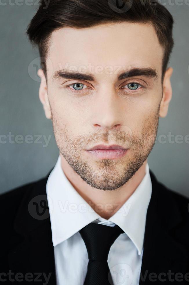 retrato de confianza y masculinidad. apuesto joven mirando a la cámara mientras está de pie contra el fondo gris foto