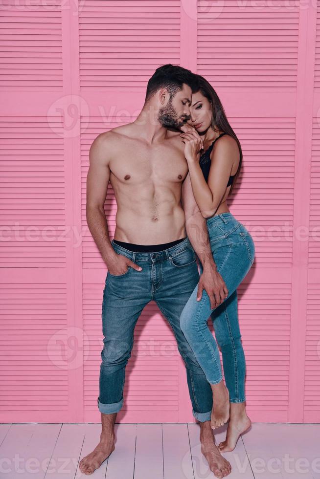 She means everything to him. Full length of beautiful young couple embracing while standing against pink background photo