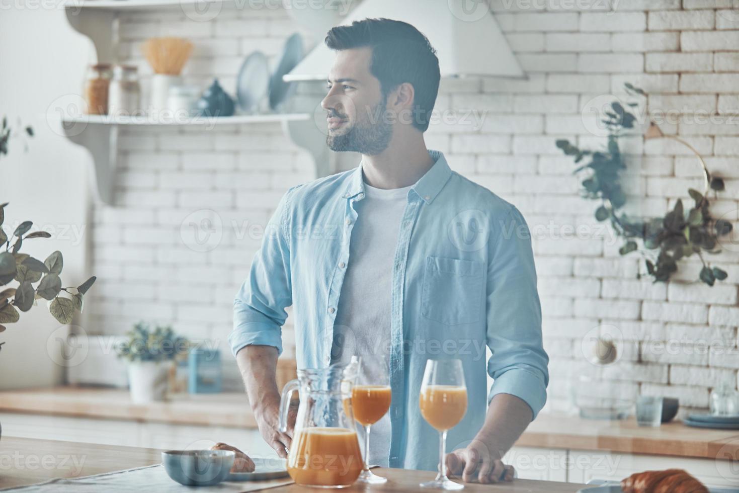 apuesto joven disfrutando del desayuno mientras pasa tiempo en la cocina doméstica foto