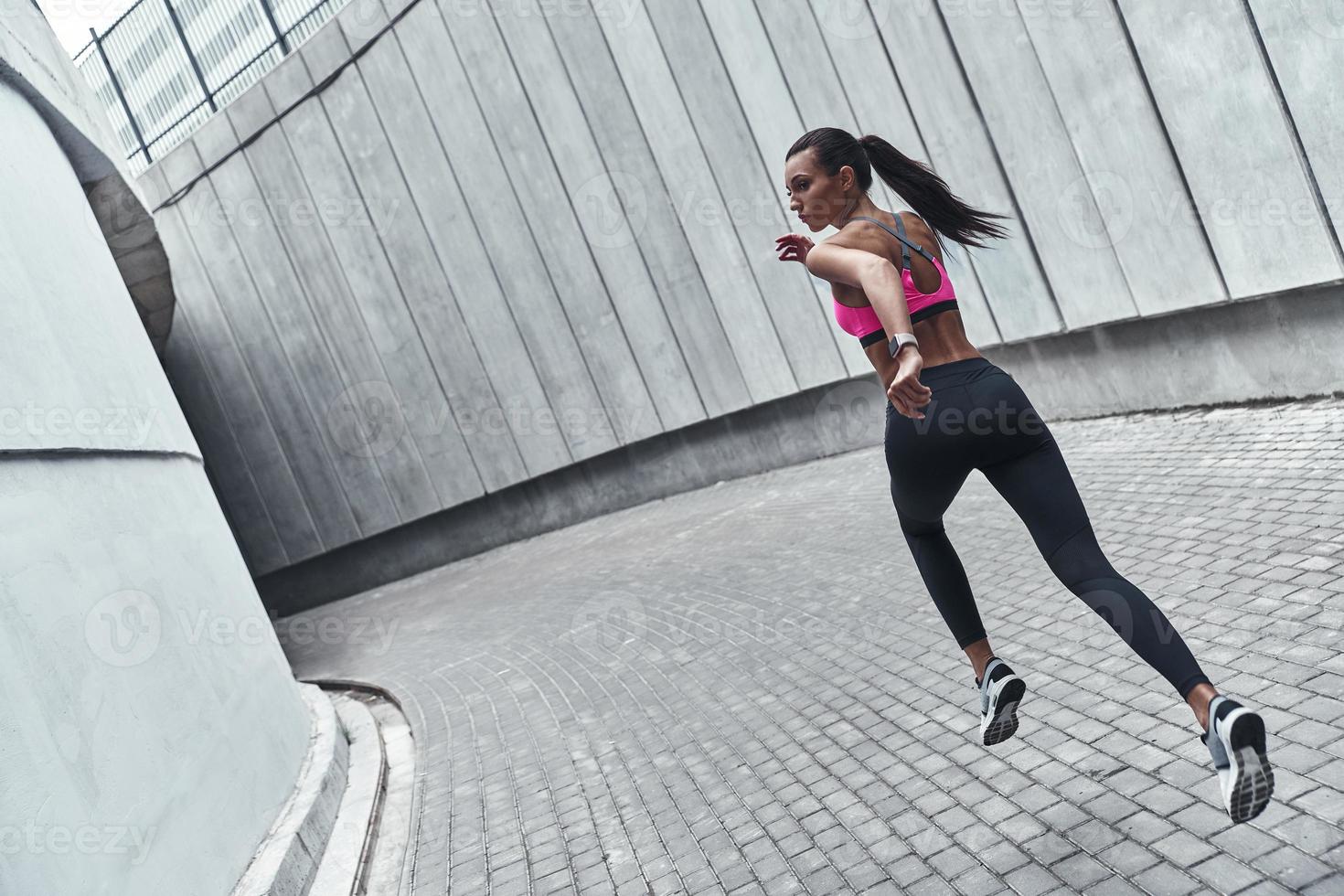 decidido a ganar. toda la longitud de una mujer joven con ropa deportiva trotando mientras hace ejercicio al aire libre foto