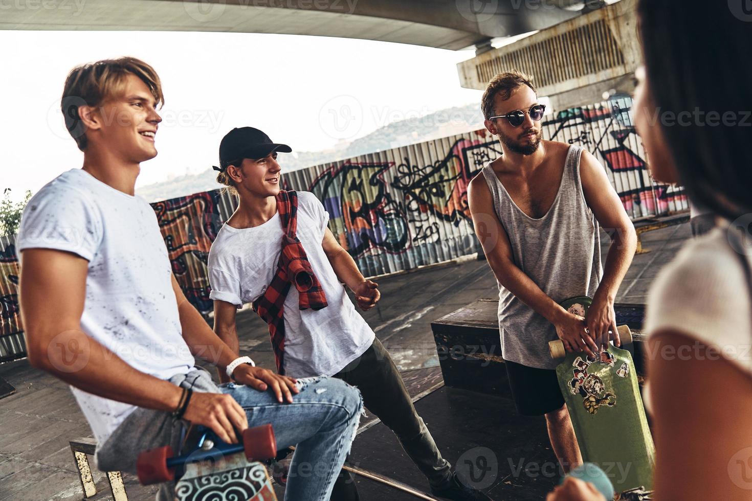 Great day with friends. Group of skater friends having a discussion while standing under the bridge outdoors photo