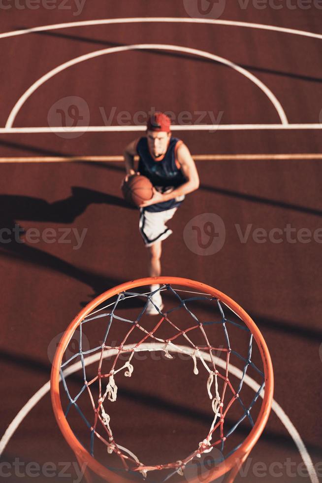 Always aimed to win. Top view of young man in sports clothing preparing to score a slam dunk while playing basketball outdoors photo